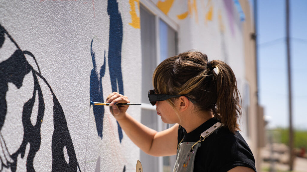 A woman painting the mural Migration: a Natural Act